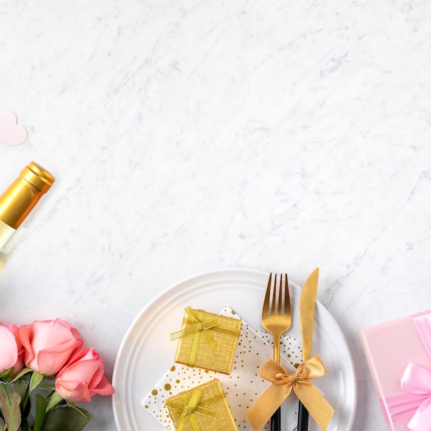 White plate with gift and pink rose flower on marble white table background for Valentine's Day special holiday dating meal concept.