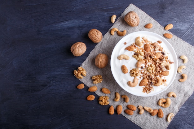 White plate with greek yogurt, granola, almond, cashew, walnuts  on black wooden background. 