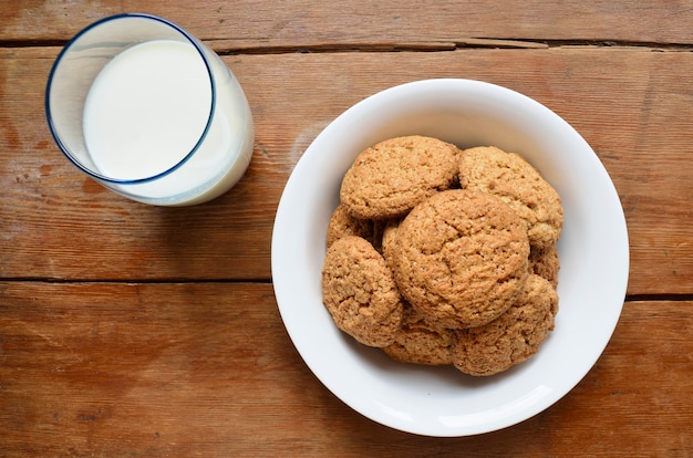 White plate with oat cookies and glass with milk on wooden table
