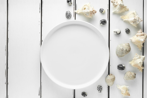 Photo white plate with seashells on white wooding background, wallpaper