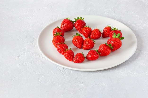 White plate with strawberries in a heart shape, concept of Valentine's Day, top view, copy space