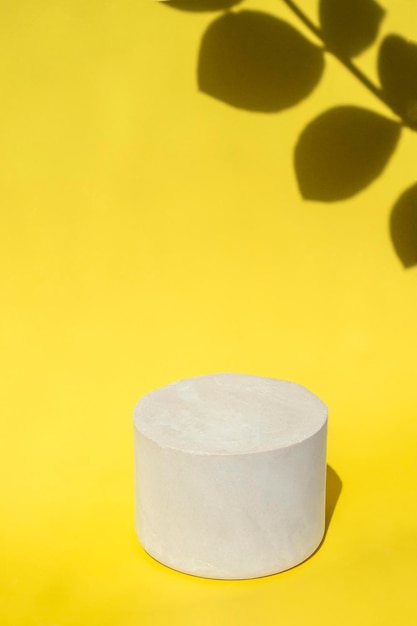 White podium close up on a yellow background with hard shadows of tropical plants Vertical Format