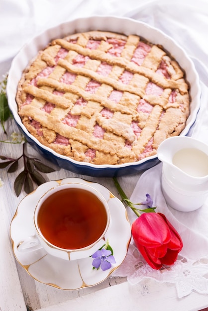 White porcelain cup of tea and freshbaked pie English breakfast stilllife with drink and treats red tulip flower and white tablecloth