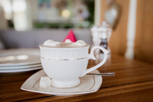 A white porcelain cup with cappuccino coffee stands on a table in a bar