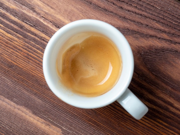 A white porcelain cup with coffee in it on a wooden background The foam is brown on the sides of the cup A flavorful invigorating breakfast drink Top view flat lay