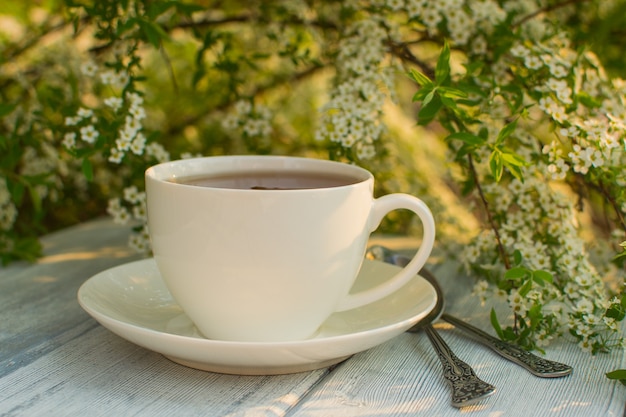 White porcelain cup with tea on a wooden table against a background of white flowers