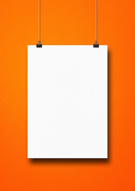 White poster hanging on an orange wall with clips.