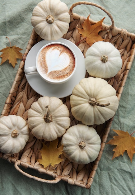 White pumpkins coffee and autumn leaves on a wicker tray