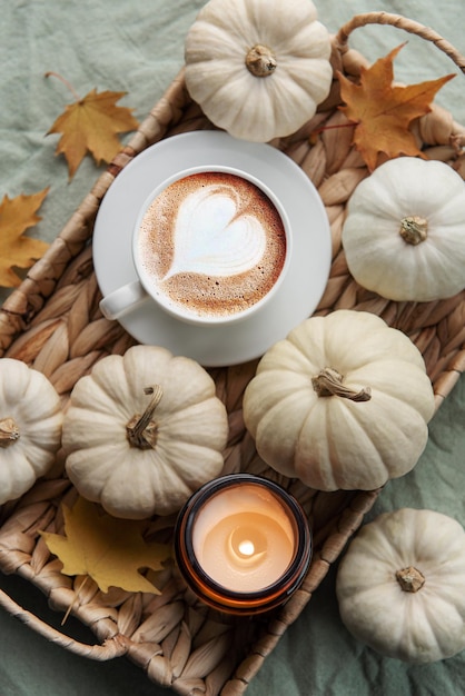 White pumpkins coffee and autumn leaves on a wicker tray