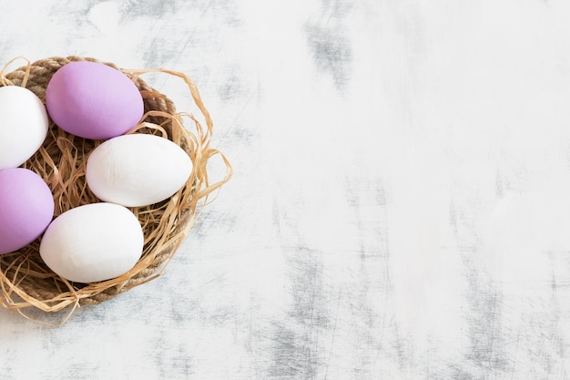 White and purple Easter eggs lying on a tray made of twine under them hay