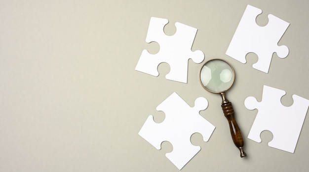 White puzzles around a magnifying glass on a gray background. concept of searching for talented people, recruiting personnel, identifying those capable of career advancement