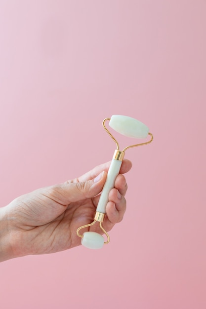 White quartz massager on a womans hand on a pink background massager to tighten the skin on