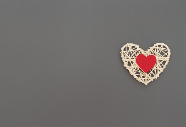 White rattan heart with red heart on grey.