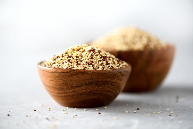 White and red raw organic quinoa in wooden bowl and rosemary on grey background. Healthy food ingredients. 