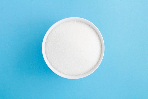 White refined sugar in white ceramic bowl on the blue background Top view