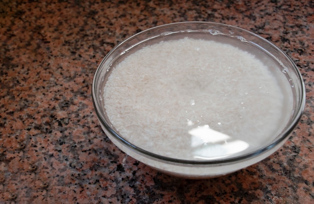 White rice soaked in water ready to cook in a bowl.