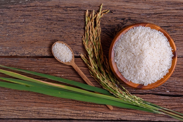 White rice (Thai Jasmine rice) in wooden bowl with unmilled rice on old wooden background.