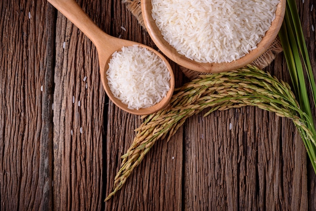 white rice in wooden bowl and unmilled rice on wooden background