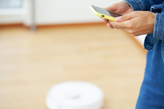 White robotic vacuum cleaner cleaning the floor while woman sitting near wall and rest