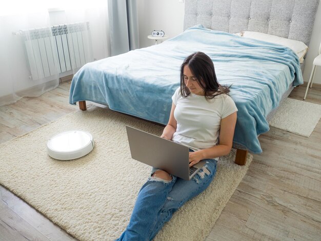 White robotic vacuum cleaner cleaning the floor while woman using laptop