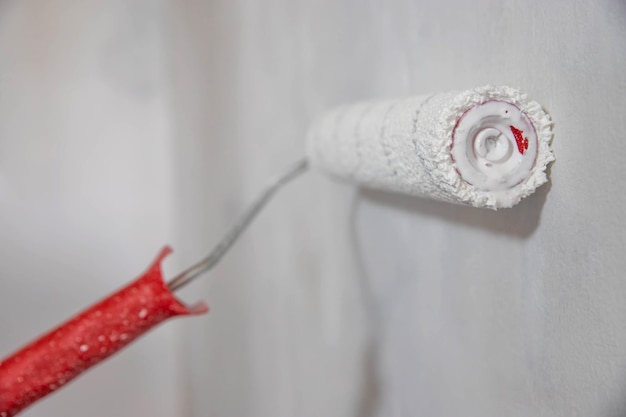 A white roller on a long red handle paints the wall white horizontal format