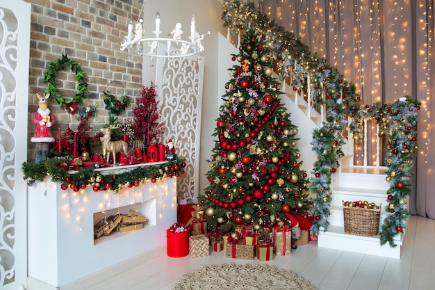 White room interior in red tones with New Year tree decorated, present boxes and artificial fireplace