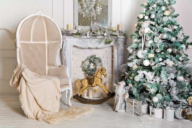 White room interior with New Year tree decorated, present boxes and artificial fireplace