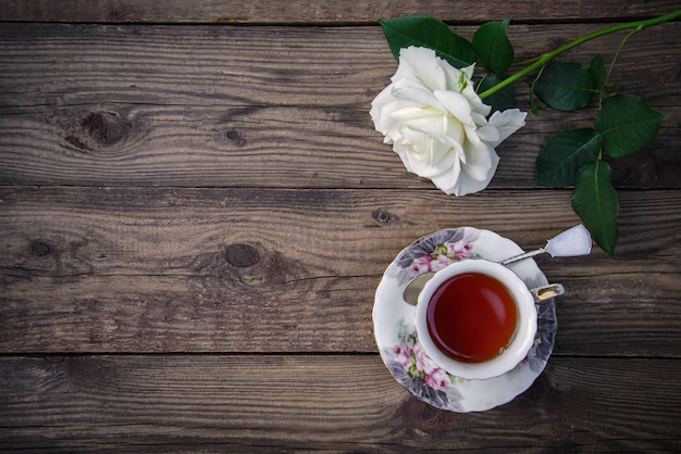 White rose and a cup of tea on a wooden background