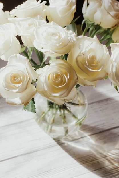 White roses stand in a vase on white wooden boards