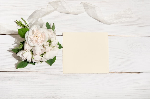 White roses with empty card on white table. Top view