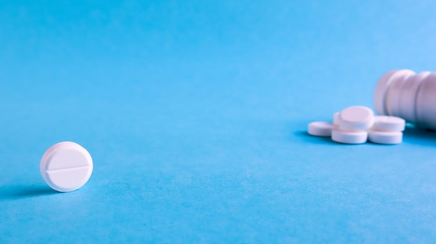 White round medical pills on a blue background. Scattered white pills on the table. The concept of medicine, pharmacy and healthcare. Copy space Empty space for text or logo.