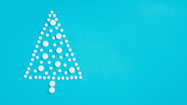 White round pills, laid out in shape of Christmas tree on light blue background. Banner. Flat lay, copy space