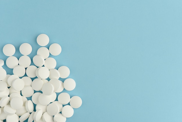 White round pills scattered on blue background. Medicine flat lay with copy space.