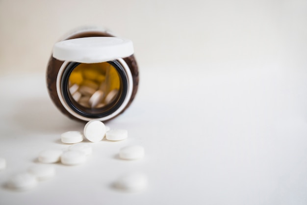 Photo white round pills spilling from an open brown bottle on white background