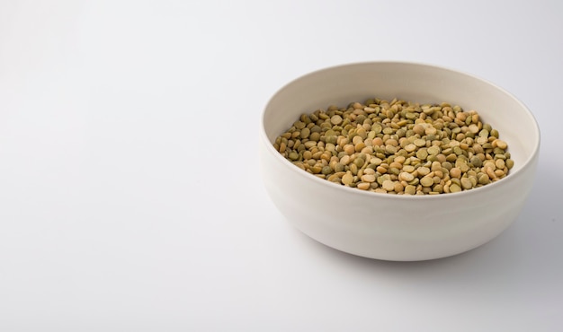 White round plate full of uncooked green lentils. isolated on white.