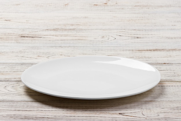 White Round Plate on white wooden table background. Perspective view