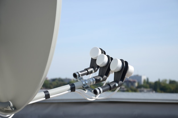 White satellite dish with three converters mounted on residental building rooftop concrete wall. Satellite television advertisement