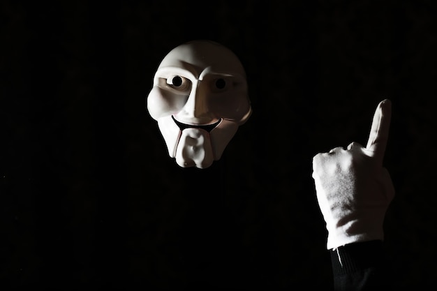 White scary mask on a black background with whites hands.