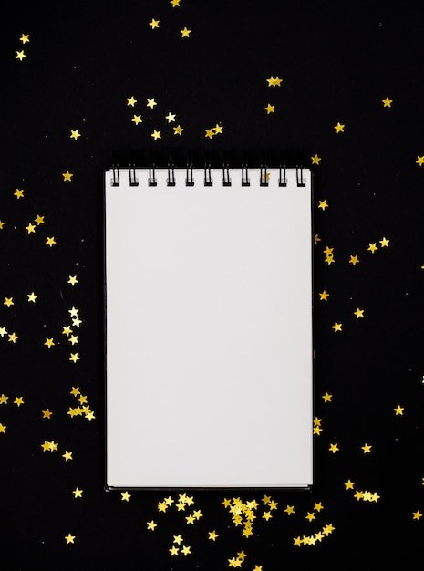  White scetchbook on black abstract background with golden stars confetti.Horizontal top v