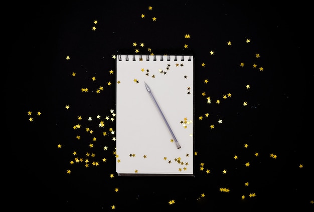 White scetchbook on black abstract background with golden stars confetti.Horizontal top vi