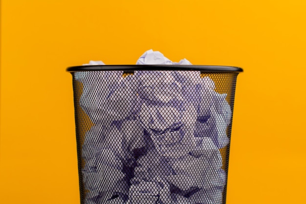 White scraps of paper in the trash can on a yellow background waste paper waste concept