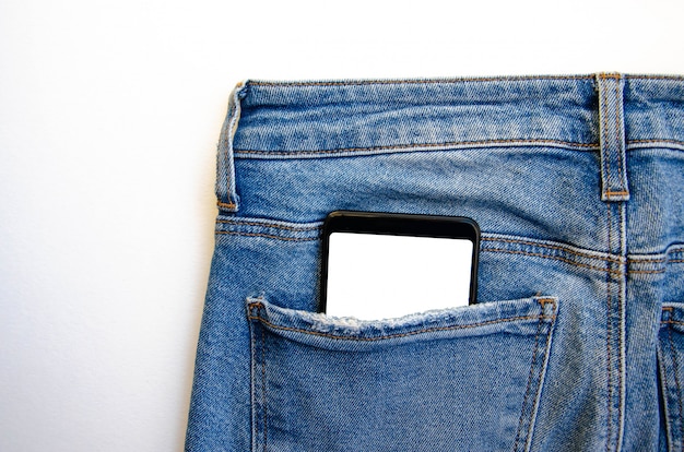 White screen smartphone in jeans pocket. Smartphone place for text. Smartphone in a pocket on a white table.