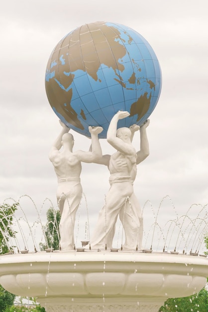 White sculptures of men holding the globe with a fountain in the sunlight