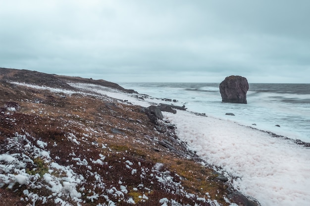 Photo white sea foam on the shore. storm on the white sea, dramatic landscape with waves rolling on the shore.