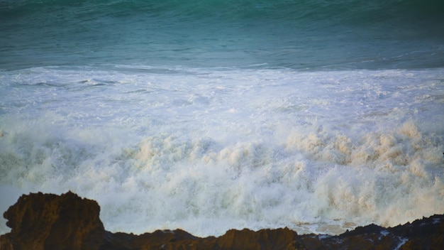 White sea waves hitting rocks beach in slow motion foaming stormy ocean rolling