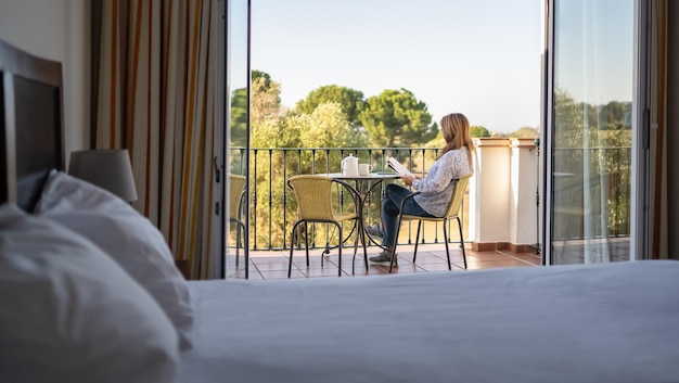 White senior woman reading a book on the terrace of her hotel room on vacation