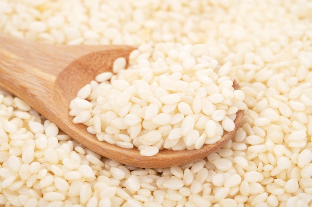 White sesame seeds organic in wooden spoon on white background. Health food concept.