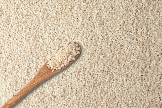 The white sesame seeds in a wooden spoon on a background full of white sesame seeds