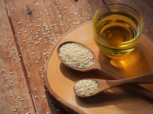 White sesame seeds in wooden spoon and a glass of sesame oil for healthy food concept.