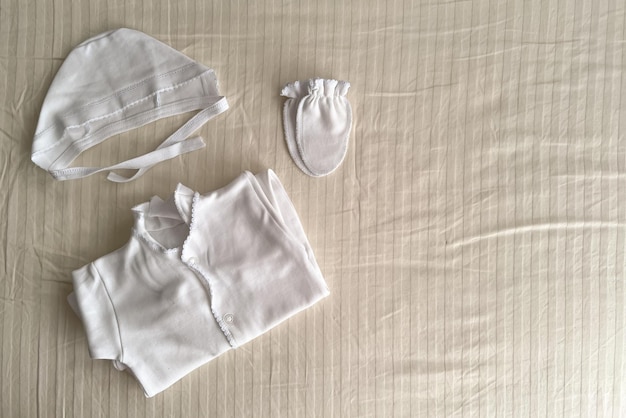 The white set for the discharge from the maternity hospital of the child is laid out on a light sheet Children's white overalls scratches and a cap Discharge of newborns